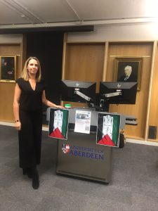 A photo of Dr Julie McDonald in the Suttie Centre conference room surrounded by Palestinian flags, the white stripe of the flag in the shape of overalls of a healthcare workers.